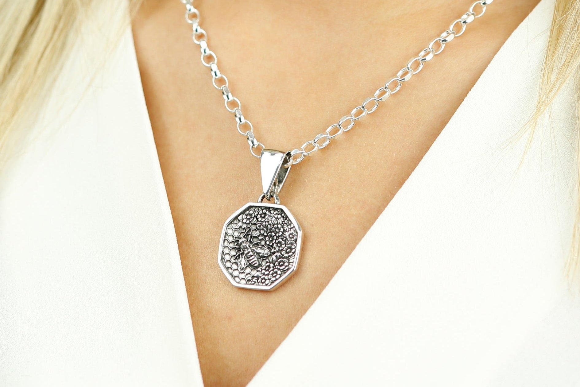 Silver necklace with a detailed pendant on a person's neck against a white background
